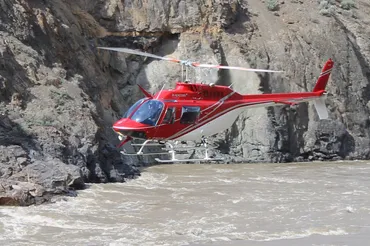 A helicopter flies low and fast through a steep river canyon